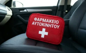 Κόκκινο τσαντάκι φαρμακείο αυτοκινήτου με λευκό σταυρό και την επιγραφή ΦΑΡΜΑΚΕΙΟ ΑΥΤΟΚΙΝΗΤΟΥ τοποθετημένο σε κάθισμα αυτοκινήτου.